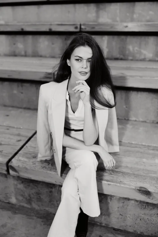 confident woman in white suit sitting on concrete stairs black and white business portrait with serious expression