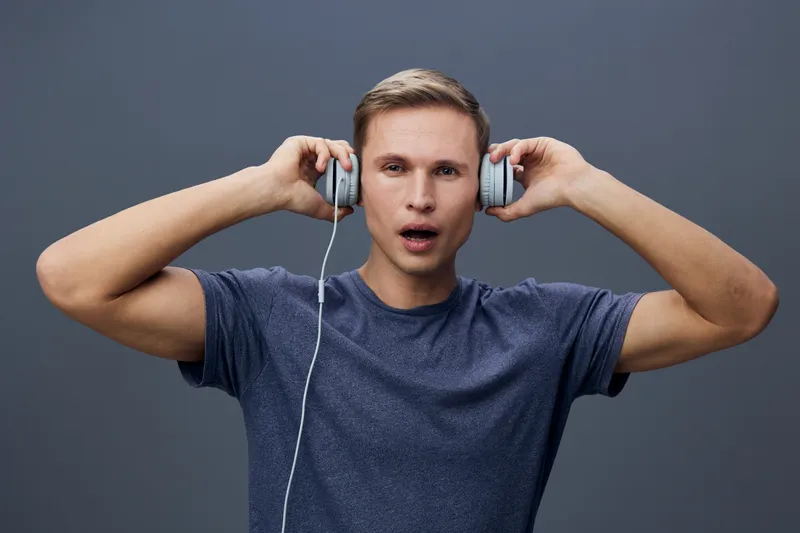 Man wearing casual t-shirt with headphones listening to music, expressing surprise or amazement, isolated on plain gray background, studio portrait, lifestyle concept, digital illustration, vibrant co