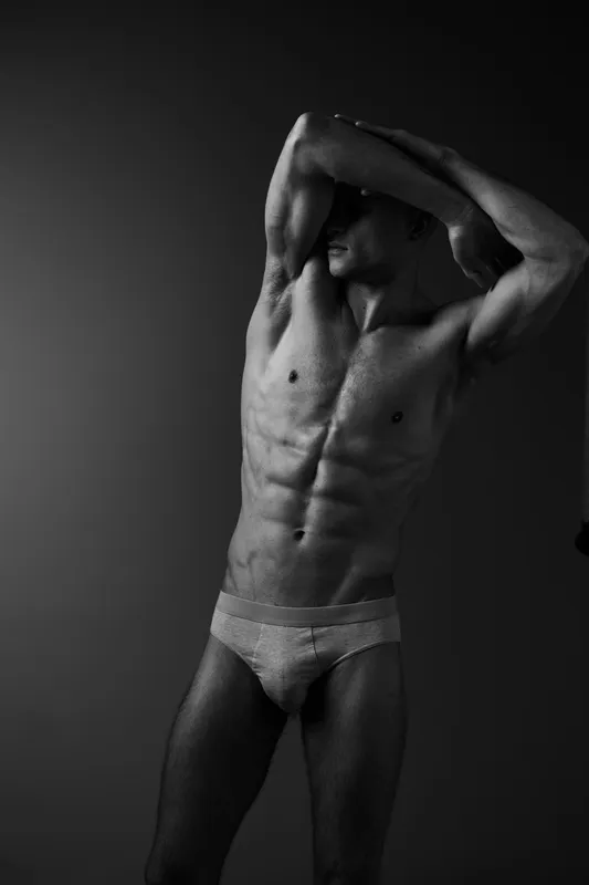 Athletic man posing in an artistic black and white photograph, showcasing strong muscles and balance, emphasizing the beauty of the human form.
