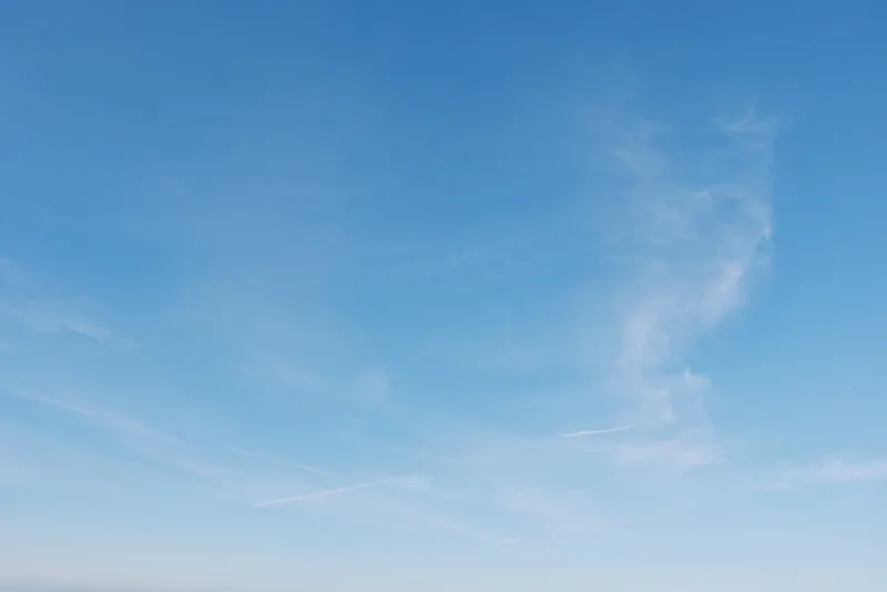 Clear blue sky with wispy clouds drifting above an open space horizon, creating a serene daytime scene suitable for nature and atmospheric background imagery.