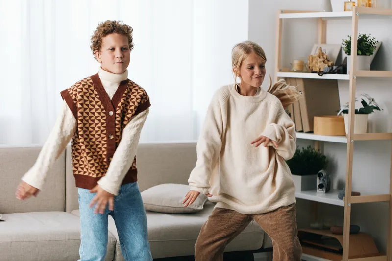 Authentic scene of playful movement at home, featuring a school aged child and adult dancing, casual knitwear, candid moment, wholesome lifestyle.