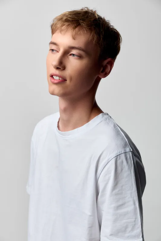 Young man in a white t shirt with a thoughtful expression, studio lighting and neutral backdrop, casual pose for fashion, lifestyle or creative projects