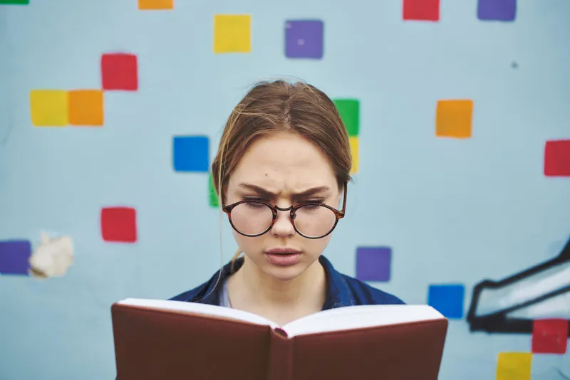 Удивленная студентка в очках на улице с книгой, эмоции, модель