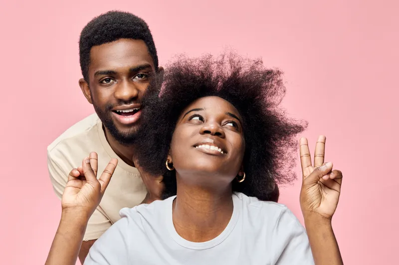 Young African couple playfully posing against a pink background, showcasing joyful expressions and casual outfits, reflecting love and friendship