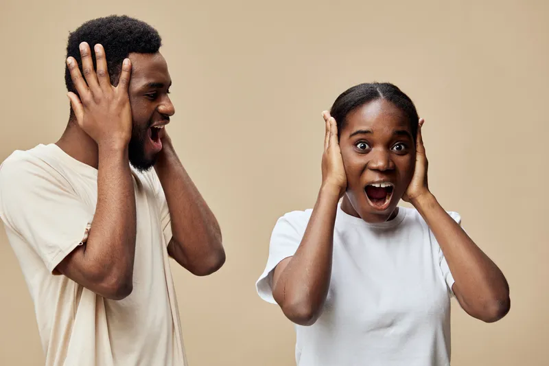 Two surprised young adults expressing shock and excitement against a beige background, showcasing diverse emotions and vibrant energy