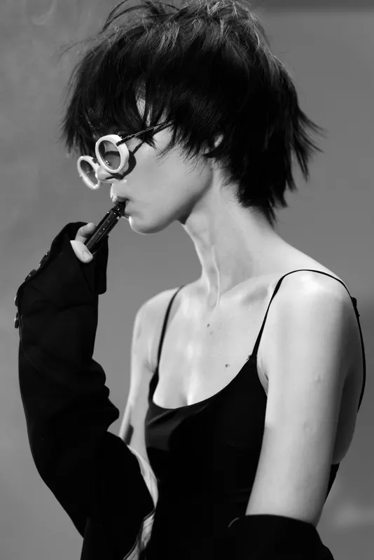 Black and white portrait of a woman wearing stylish glasses and a sleeveless dress in a contemplative mood.