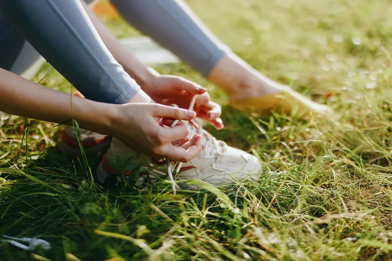 Young woman tying shoelaces on running shoes in a sunny park, representing an active lifestyle with nature background and bright colors, perfect for fitness themes