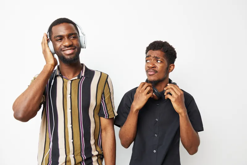 Young African American men enjoying music with headphones, expressing different emotions. One smiles while the other looks curious and interested.