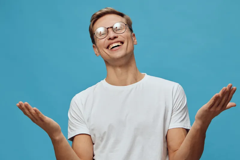 smiling young man wearing glasses white t-shirt expressing joy blue background concept mental health gadgets positive emotion