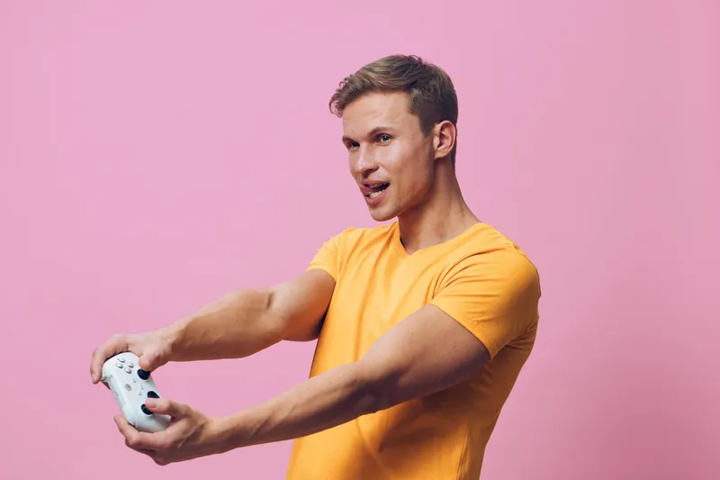 young caucasian man wearing orange t-shirt play game using wireless controller excited expression pink background digital entertainment concept