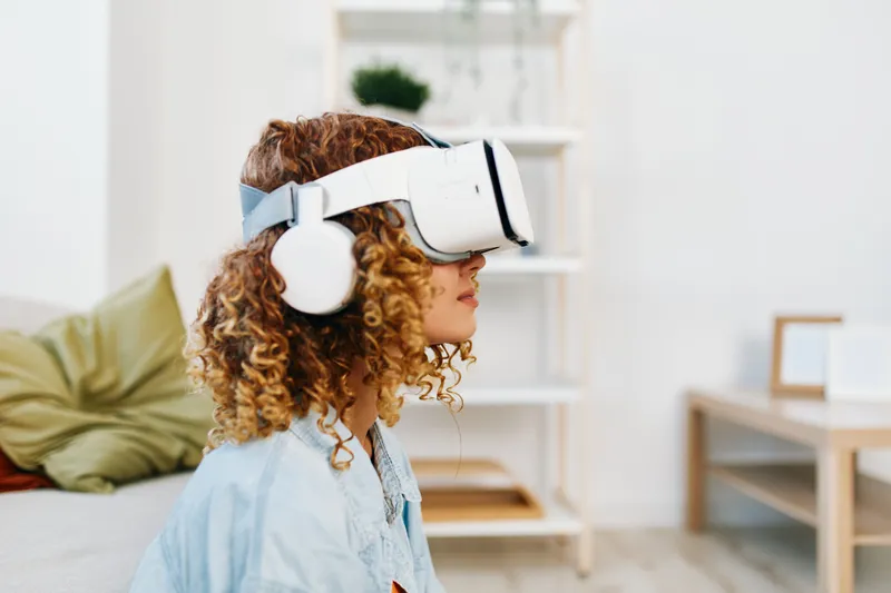 Улыбающаяся женщина наслаждается игрой в виртуальной реальности с VR-очками у себя дома