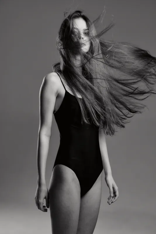 Black and white portrait of a woman with flowing hair in a black bodysuit, expressing motion and elegance.