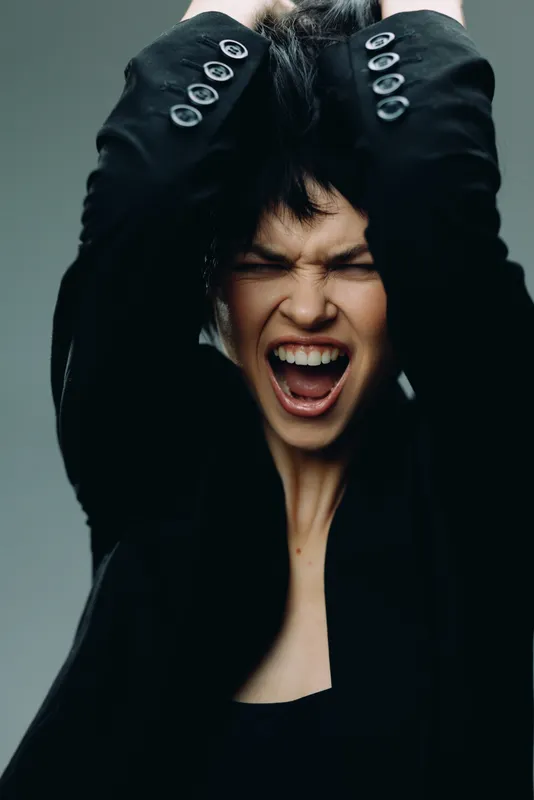 Young angry woman screaming with raised hands in black outfit with intense emotion