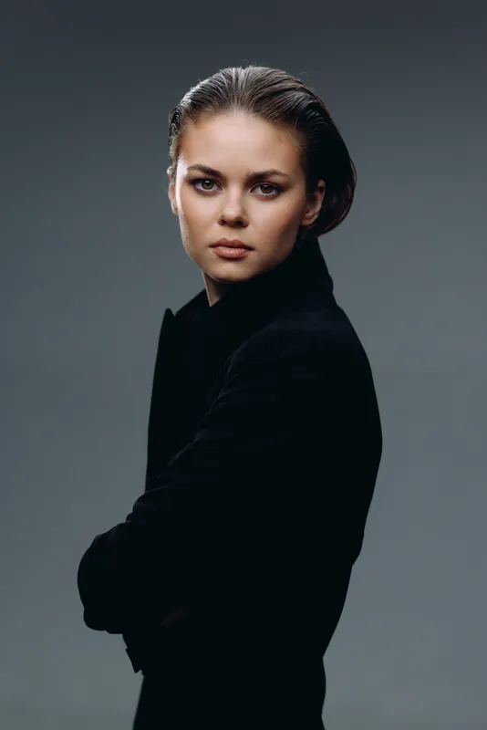 Serious woman in black turtleneck posing with folded arms against gray background, confident and thoughtful expression