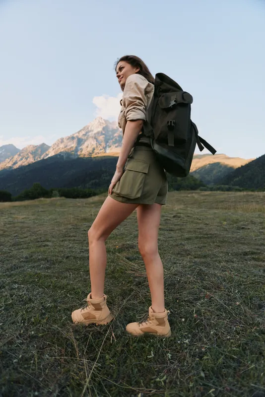 Young woman with a backpack hikes through a rugged mountain landscape, basking in warm sun, blue sky, and a gentle breeze, eyes ahead, focused and free.