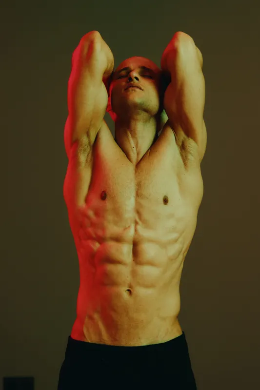 Muscular man posing under dramatic lighting with a bold color palette. His intense expression captures strength and determination, evoking emotions of empowerment. ###