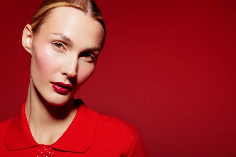 Close-up portrait of a woman with red lipstick and red clothing against a red background. Concept of beauty, fashion, makeup, and elegance with studio lighting.