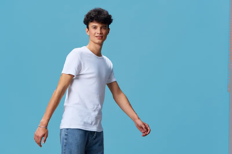 young man walking confidently wearing casual white t-shirt and jeans on bright blue background with natural expression and clean styling