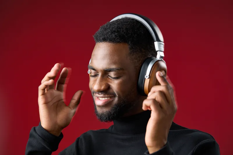 Young African man enjoying music with headphones, expressing joy and relaxation against a vibrant red background, ideal for music and lifestyle themes