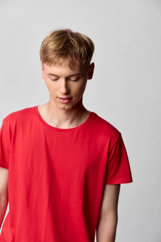 Teen boy red shirt casual clothing, downward gaze, neutral background, soft lighting, calm mood, minimal styling, suitable for youth fashion, everyday wear, studio portrait style with clean