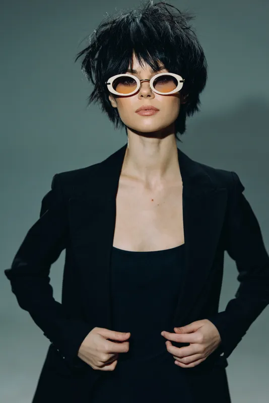 Stylish woman in black outfit and trendy sunglasses posing with confidence in studio lighting setting