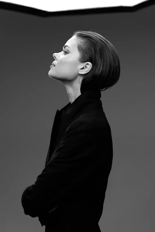 Black and white portrait of a confident woman with arms crossed looking sideways in studio lighting.