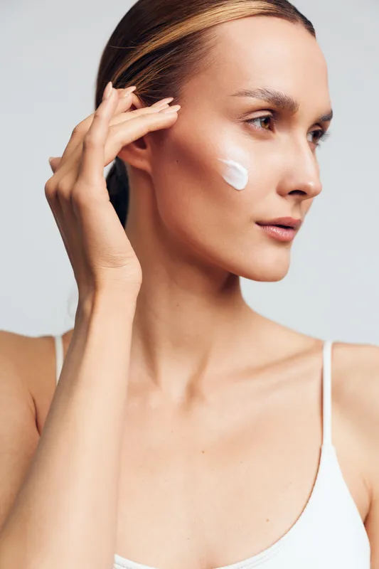 Woman skincare routine, beauty model applying white cream near eye, hand on face, fresh skin, close up portrait, self care and wellness, isolated on neutral studio background daily care