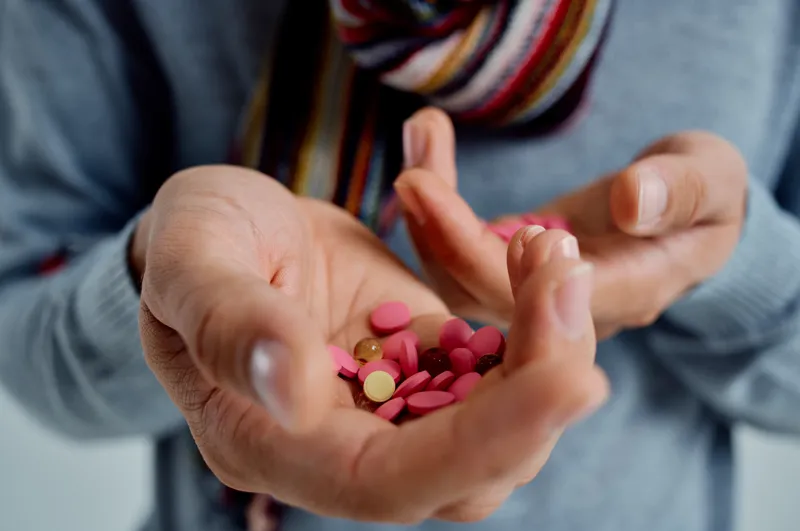 Больной мужчина в свитере держит в руке таблетки, что указывает на проблемы со здоровьем