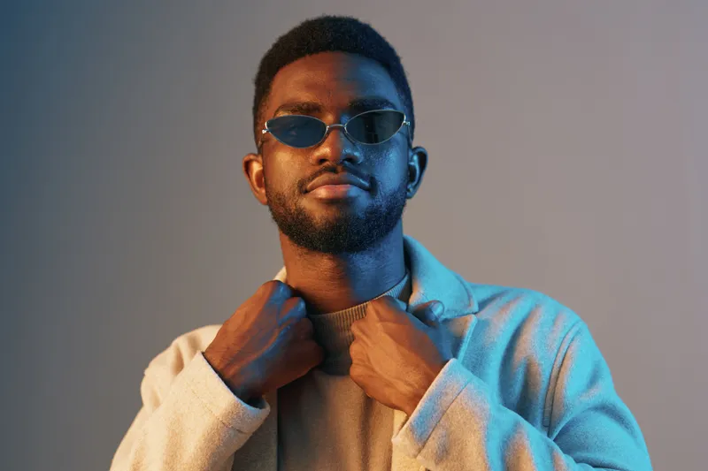 Stylish African man wearing sunglasses, looking confident against a colorful backdrop, embodying modern fashion and self expression in a casual, urban style