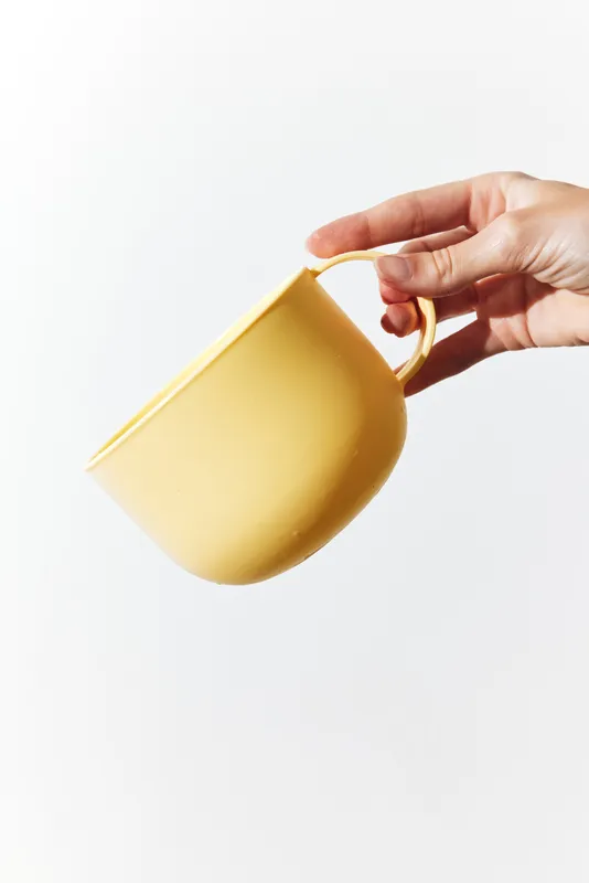 Жёлтая кружка со словом «cup» в руке на белом фоне