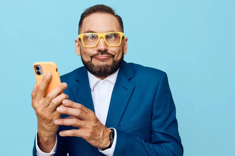 Professional man in a blue suit holds a smartphone against a bright colored background, radiating confidence and focus while engaging in business tasks.
