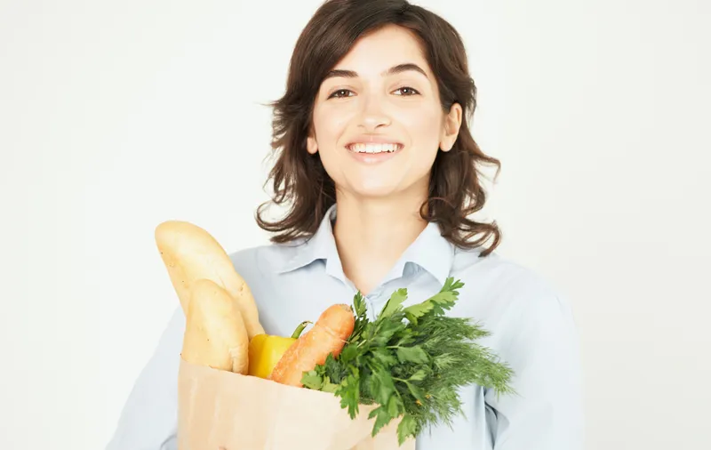 Брюнетка с пакетом продуктов: овощи, зелень, покупки в супермаркете