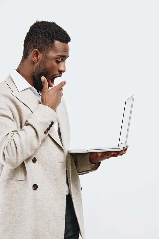 Thoughtful man in beige sweater with hand on chin looking at open laptop computer isolated on plain white background studio portrait. People lifestyle concept