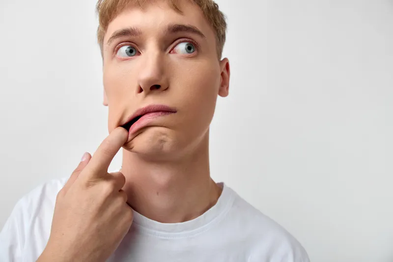 Thinking, pondering, expression by a man with finger on lips, curious and unsure look, capturing hesitation, contemplation, and inner decision in a simple studio setting