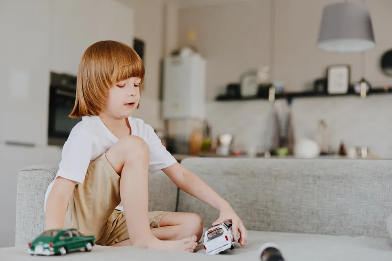 Young boy playing with toy cars indoors, focused and creative, showcasing a moment of childhood joy and imagination in a cozy living space.