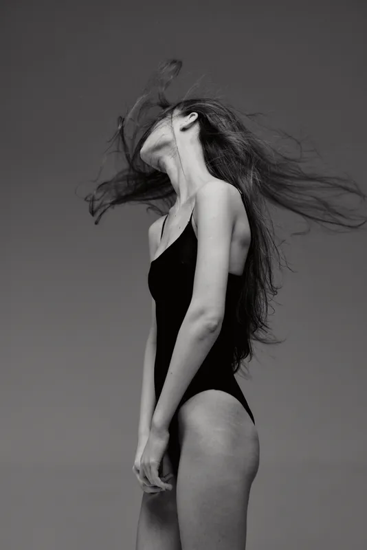 Black and white silhouette of a young woman in a swimsuit with flowing hair against a dark background