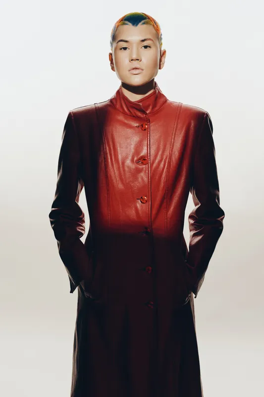 woman with short colorful hair wearing a red leather coat, standing confidently against a white background, showcasing modern fashion style and bold attitude