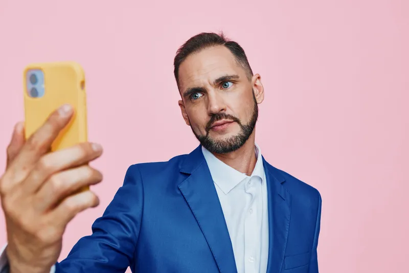 A business professional man in a blue suit takes a self portrait against a vibrant pink backdrop, showcasing confident and focused emotions in an isolated color setting.