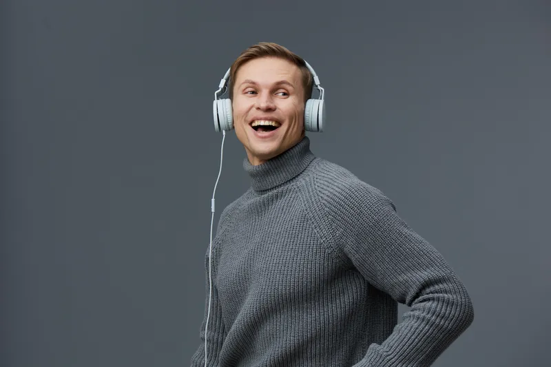 Smiling young caucasian man wearing gray knit sweater with headphones listen music digital detox concept on gray background studio portrait