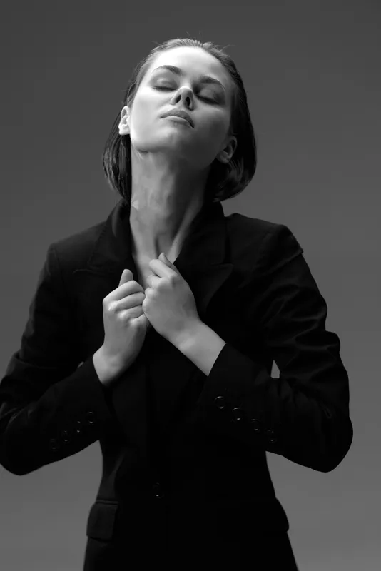 Black and white portrait of confident woman in dark jacket with closed eyes and serene expression.