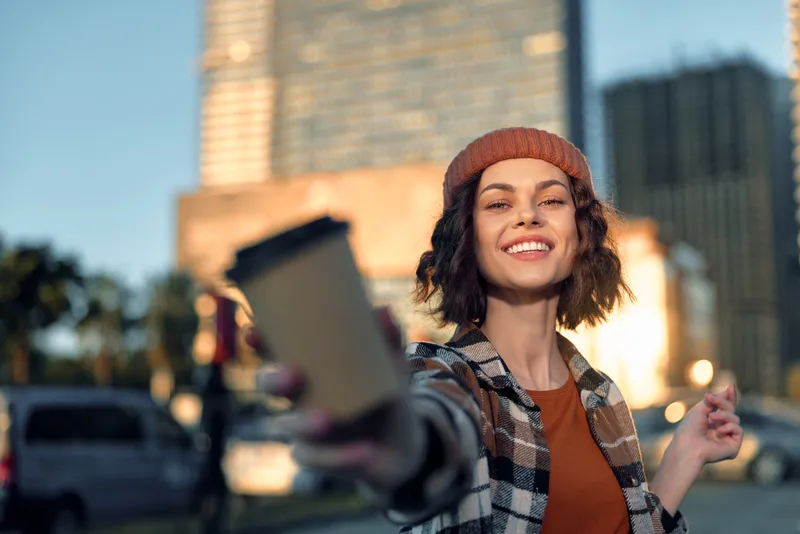 woman coffee smile urban candid authenticity lifestyle golden hour glow portrait of a happy young female offering takeaway cup on city street, emotional storytelling and mindful living vibe