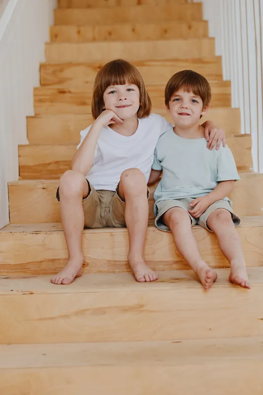 Happy children sitting on wooden stairs, enjoying a playful moment together, smiling and relaxed in a bright atmosphere for family-focused imagery.