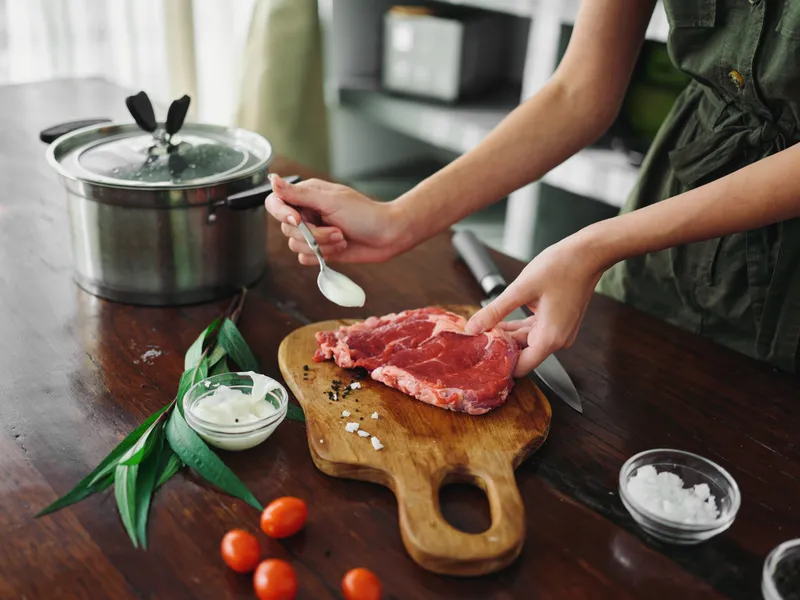 Женщина на кухне готовит ужин из мяса, овощей и специй на деревянном столе на фоне стильной кухни, крупный план рук, свежие экопродукты, образ жизни