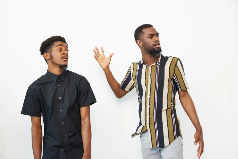 Two black men are expressing emotions in a candid moment, showcasing a mix of surprise and confusion. Their engaging poses enhance the scene’s dynamic feel.