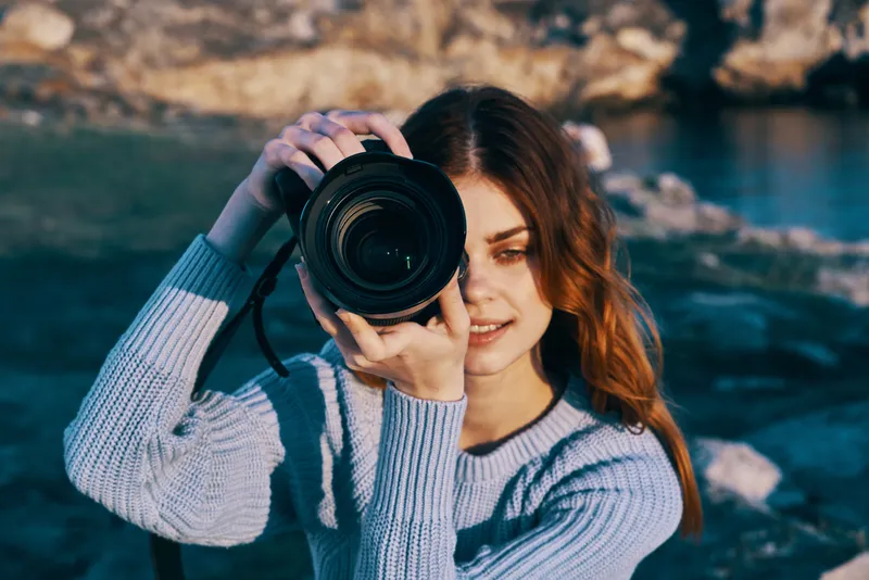 Рыжеволосая женщина-фотограф на фоне скалистых гор, профессионально работающая на природе