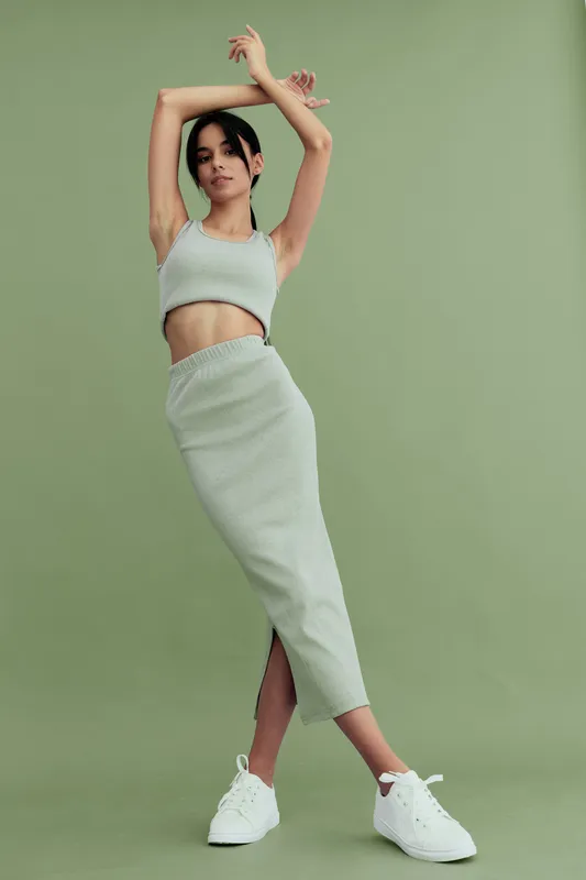 young woman posing stylishly in light green two-piece outfit with sneakers against green background, showing modern fashion and casual elegance, indoor studio setting