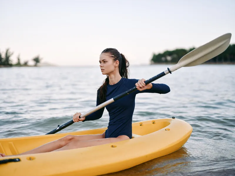 athletic woman kayaking on calm water with paddle, wearing dark sportswear, outdoor adventure and summer activity by the lake.