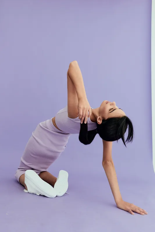 woman stretching in lavender outfit, performing yoga pose on purple background, athletic, flexible, serene, fitness practice