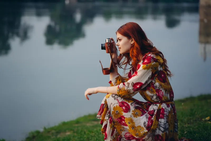 Рыжеволосая женщина с фотоаппаратом на природе, у озера