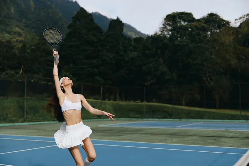 Energetic female tennis player serving on a sunny day, showcasing athleticism and focus against a lush green background